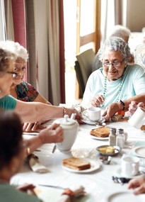 Drei ältere Frauen sitzen bei Kaffee und Kuchen gemeinsam am weissgedeckten Tisch. 