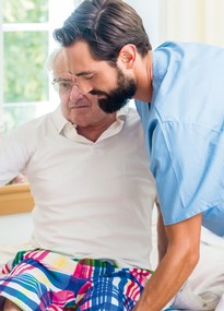 Eine männliche Pflegeperson hilft einem älteren Mann beim Lagewechsel. 