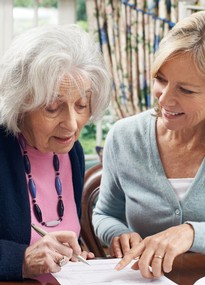 Eine Frau mittleren Alters hilft einer älteren Frau beim Ausfüllen eines Formulars. 